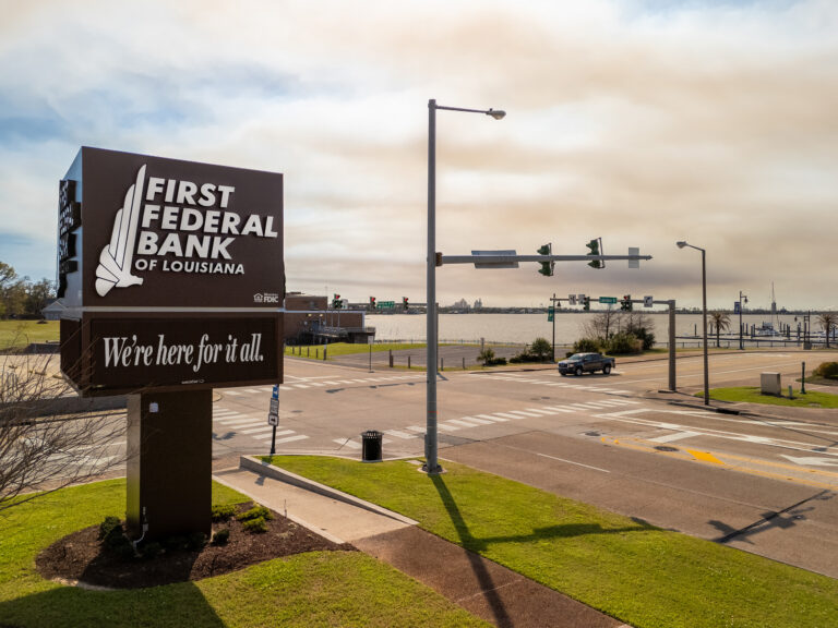 A view of the First Federal Bank of Louisiana's Main Office sign with the lake and marina in the background on a sunny day